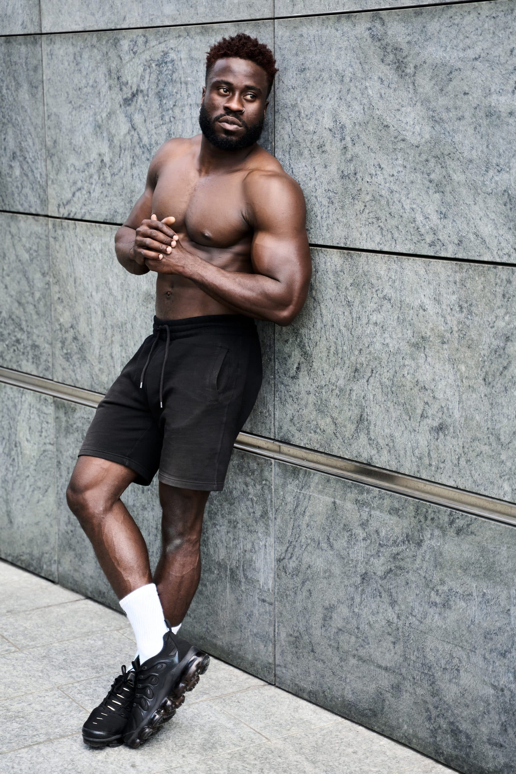 Fit strong shirtless young African black man standing at urban wall.